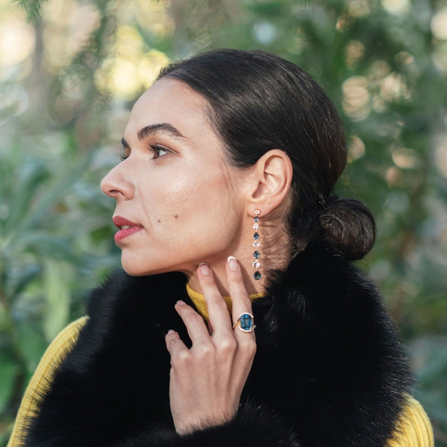 Model demonstrating the wear of the Luxury gemstone jewellery piece, the Long Teal Topaz and White Topaz Drop Earrings in 18ct Yellow Gold and the Gstaad Statement Ring – Gstaad Collection, Augustine Jewellery, Luxury Jewellery London.